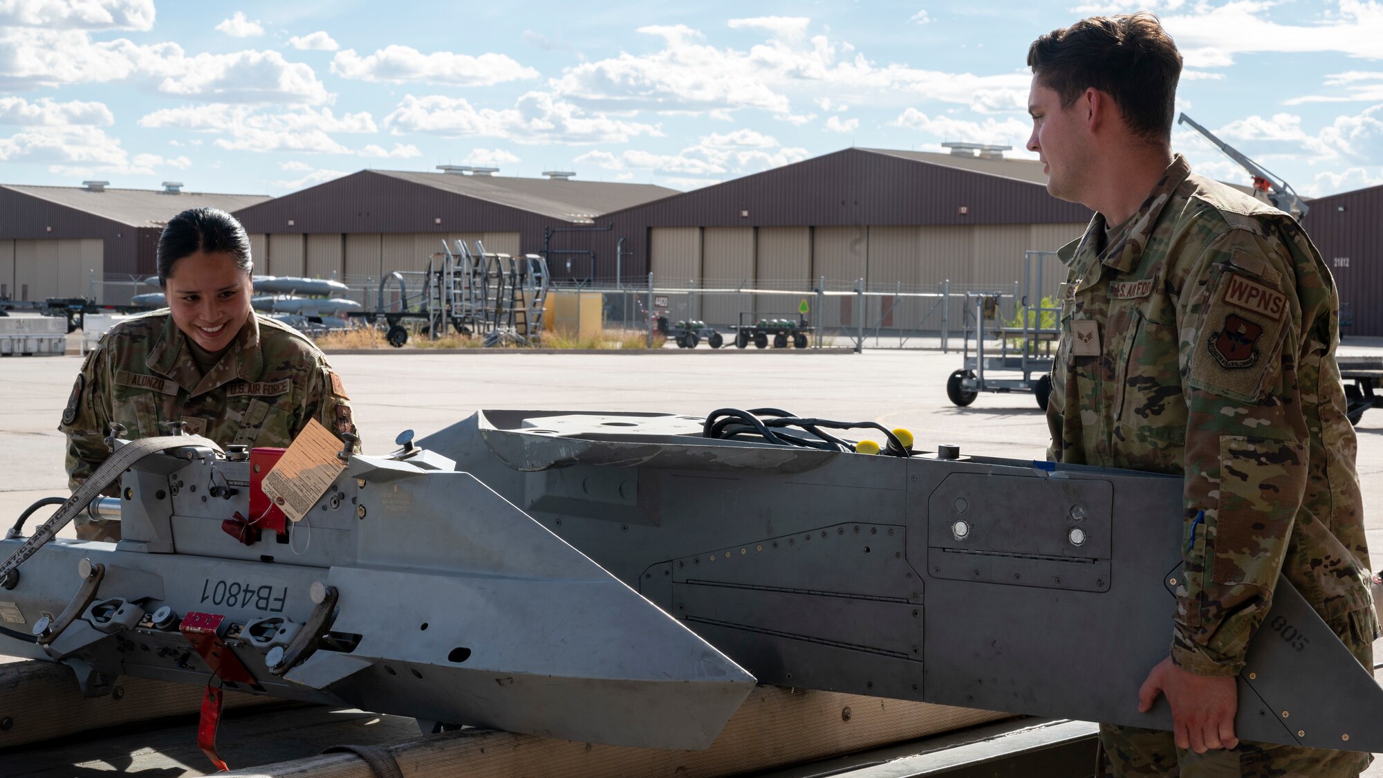 U.S. Air Force Senior Airman Kaih Alonzo, left, and U.S. Air Force Senior Airman Harrison Sizemore, 49th Equipment Maintenance Squadron load crew technicians, load a bomb rack onto a truck bed at Holloman Air Force Base, New Mexico, Oct. 10, 2023.