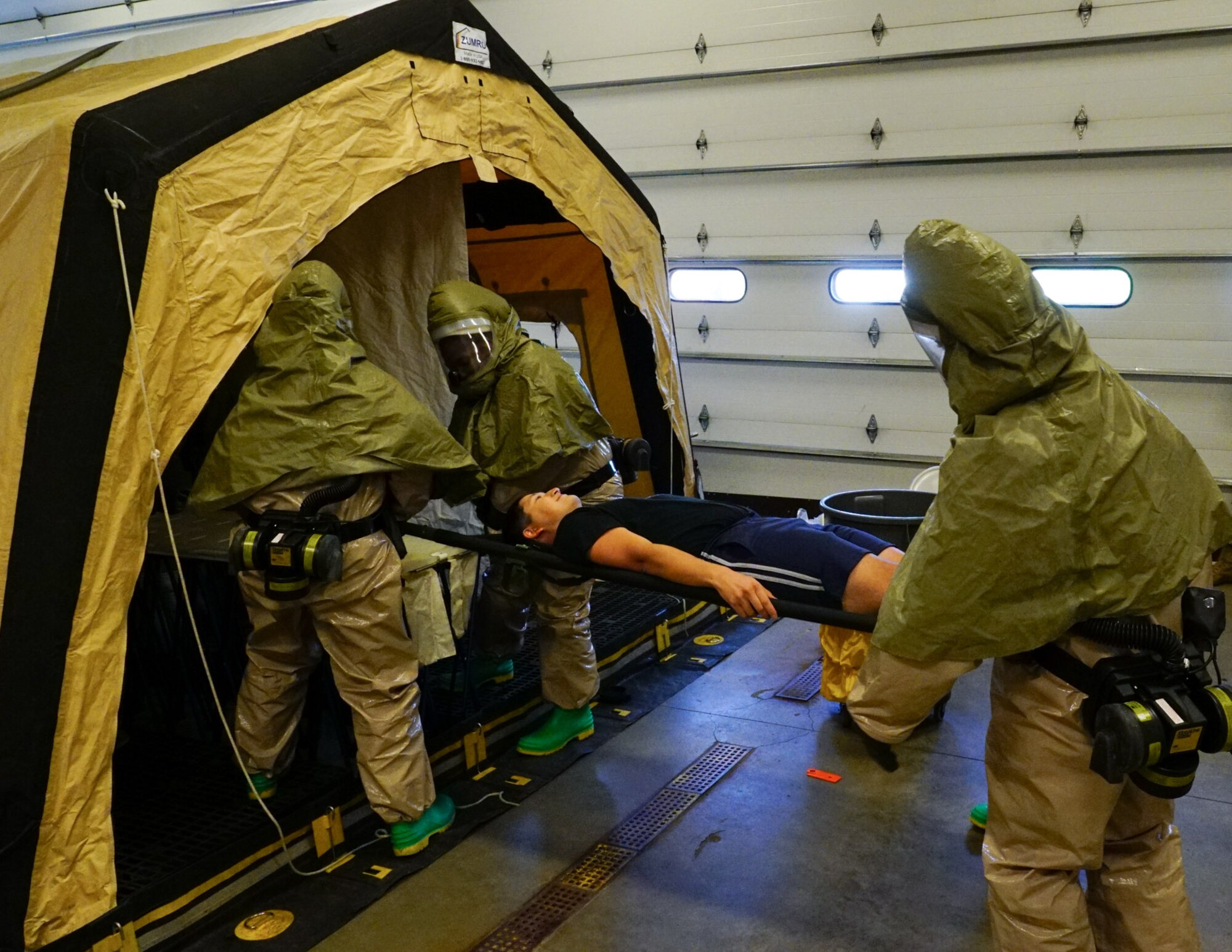 Airmen carry a volunteer patient into a tent.