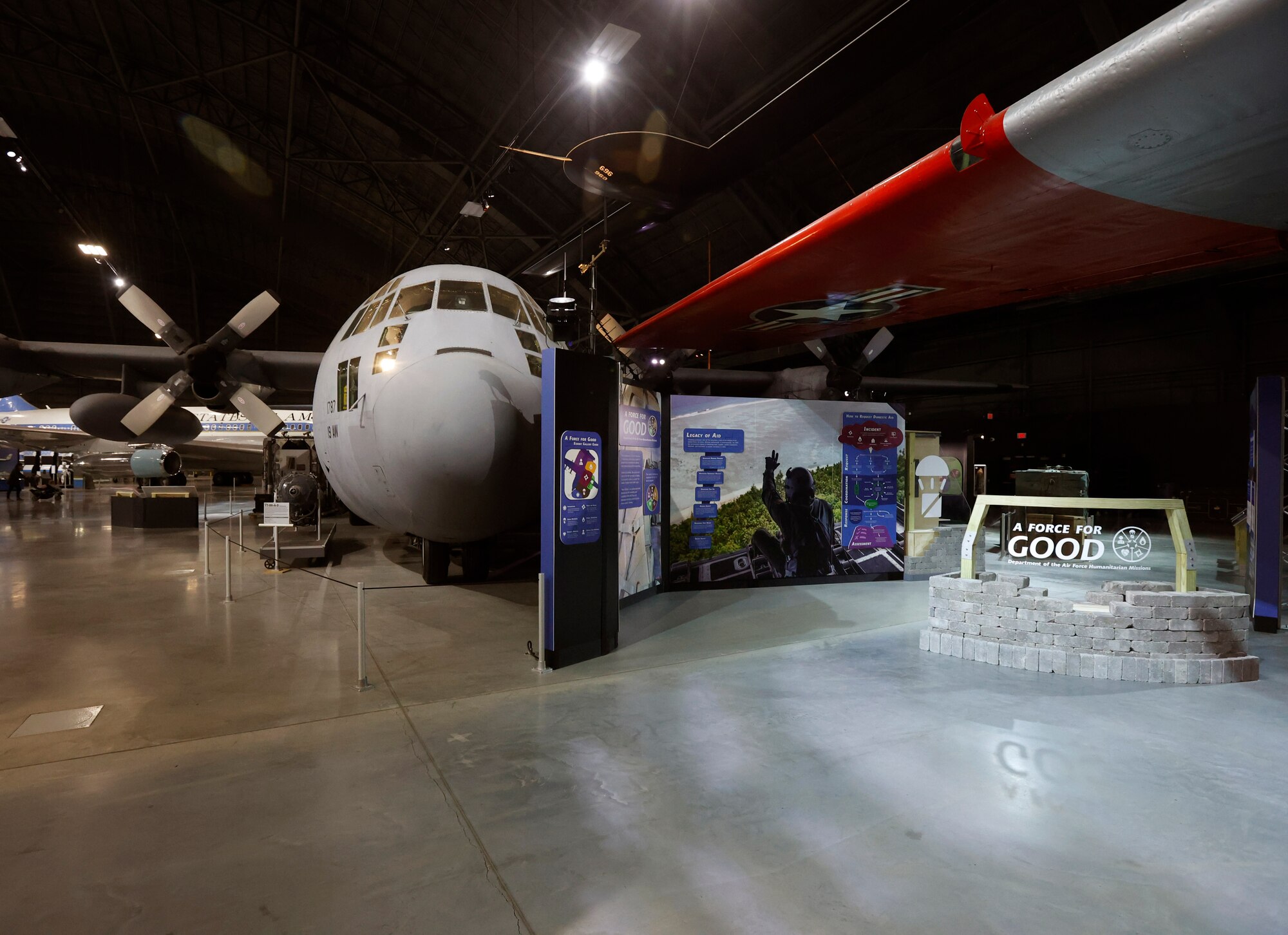 A Force for Good: Department of the Air Force Humanitarian Missions” is the museum’s latest permanent exhibit. Located in the Global Reach Gallery near the C-130E, the exhibit highlights this valuable domestic and global U.S. Air Force mission that often goes unseen to the general public. 
Image of the entrance to the Humanitarian exhibit looking at the nose of the C-130. To it's right is a blue wall with exhibit information, and to it's right is a short stone, wood and plexiglass wall with the name of the exhibit.