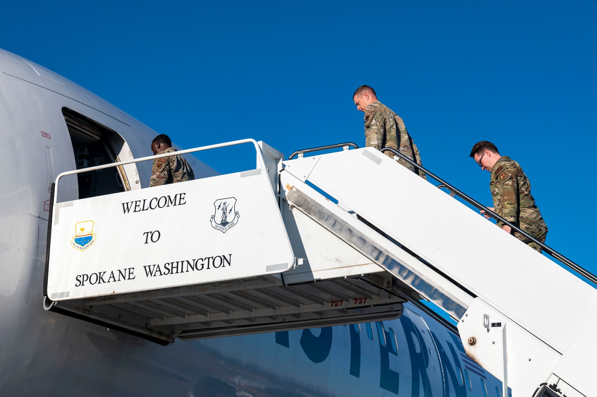 Airmen walk on air stairs to board a plane.