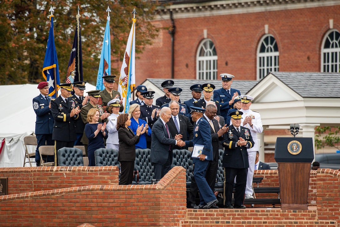 Service members and civilians in an outdoor seating area applaud.