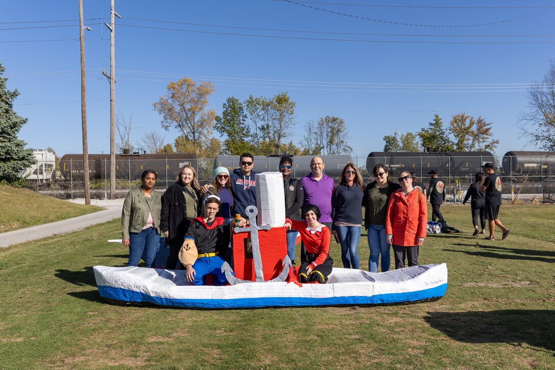 A group of smiling people in front of and on a cardboard canoe like boat.