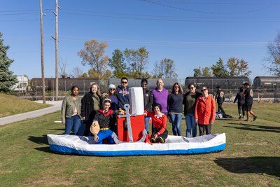 A group of smiling people in front of and on a cardboard canoe like boat.