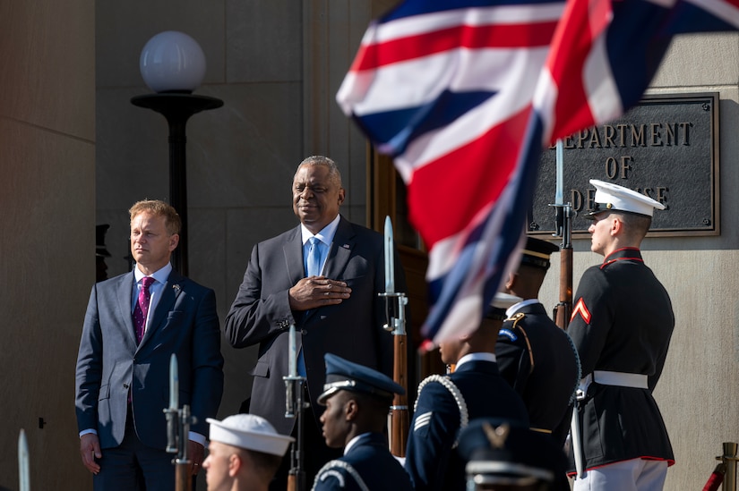 Two men stand at the top of stairs while a military honor guard greets them.