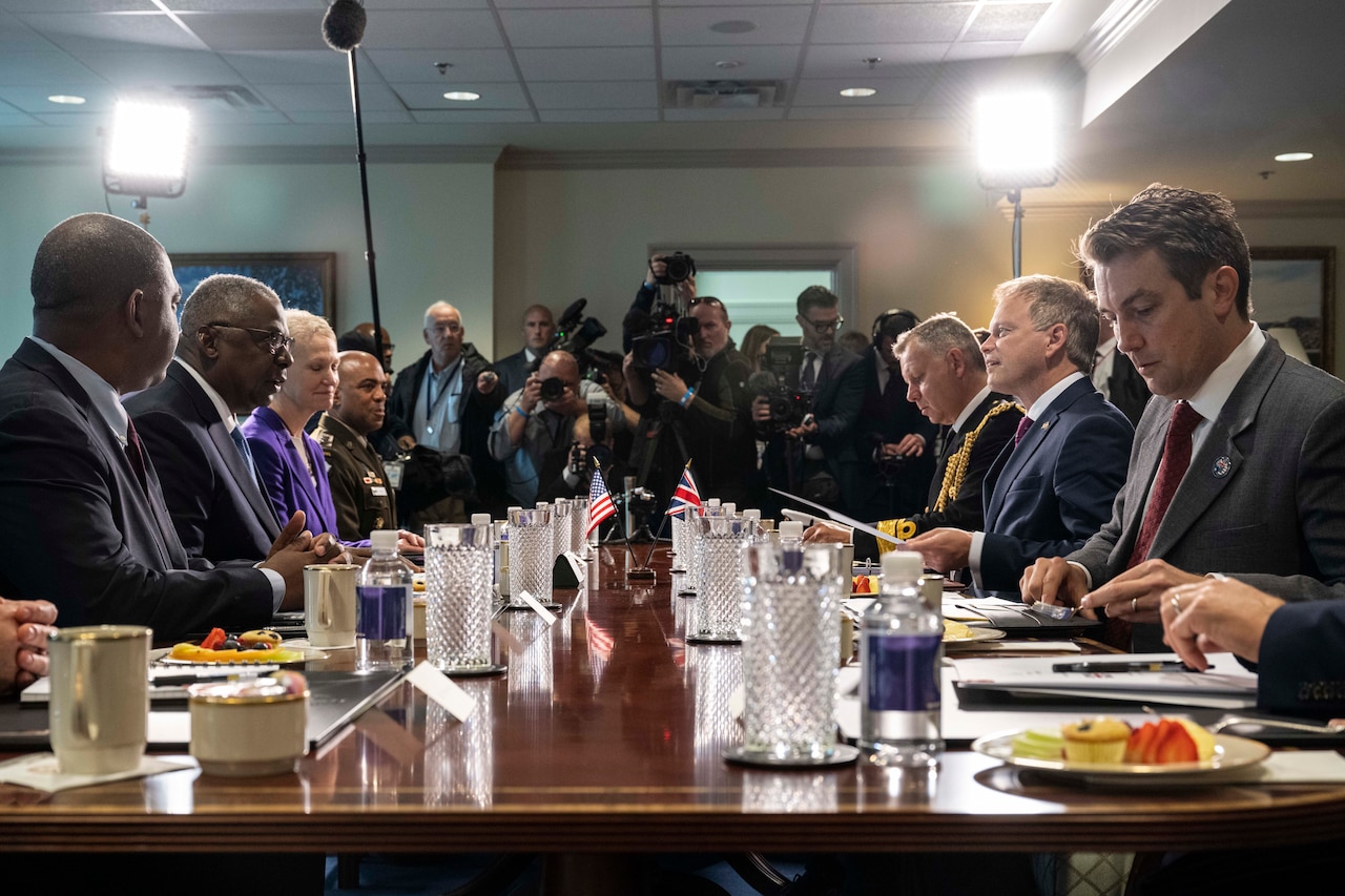 Secretary of Defense Lloyd J. Austin III and British Defense Secretary Grant Shapps sit facing each other at table as others surround them for a meeting.