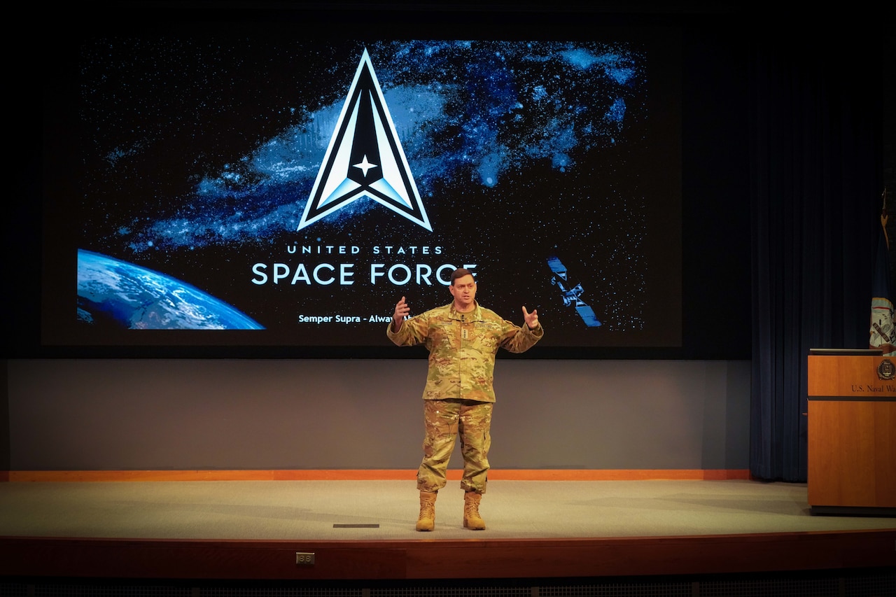 A man in uniform gestures with his hands while standing on a stage.