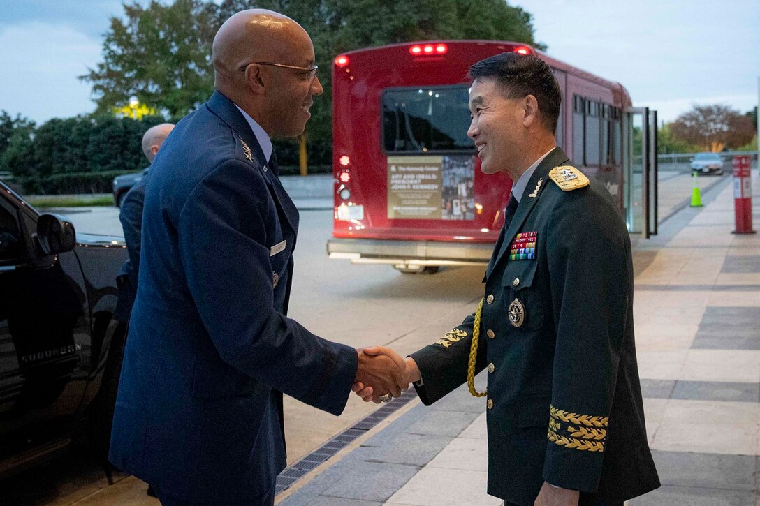 Chairman of the Joint Chiefs of Staff Air Force Gen. CQ Brown, Jr. shakes hands with another official in uniform on a city sidewalk.