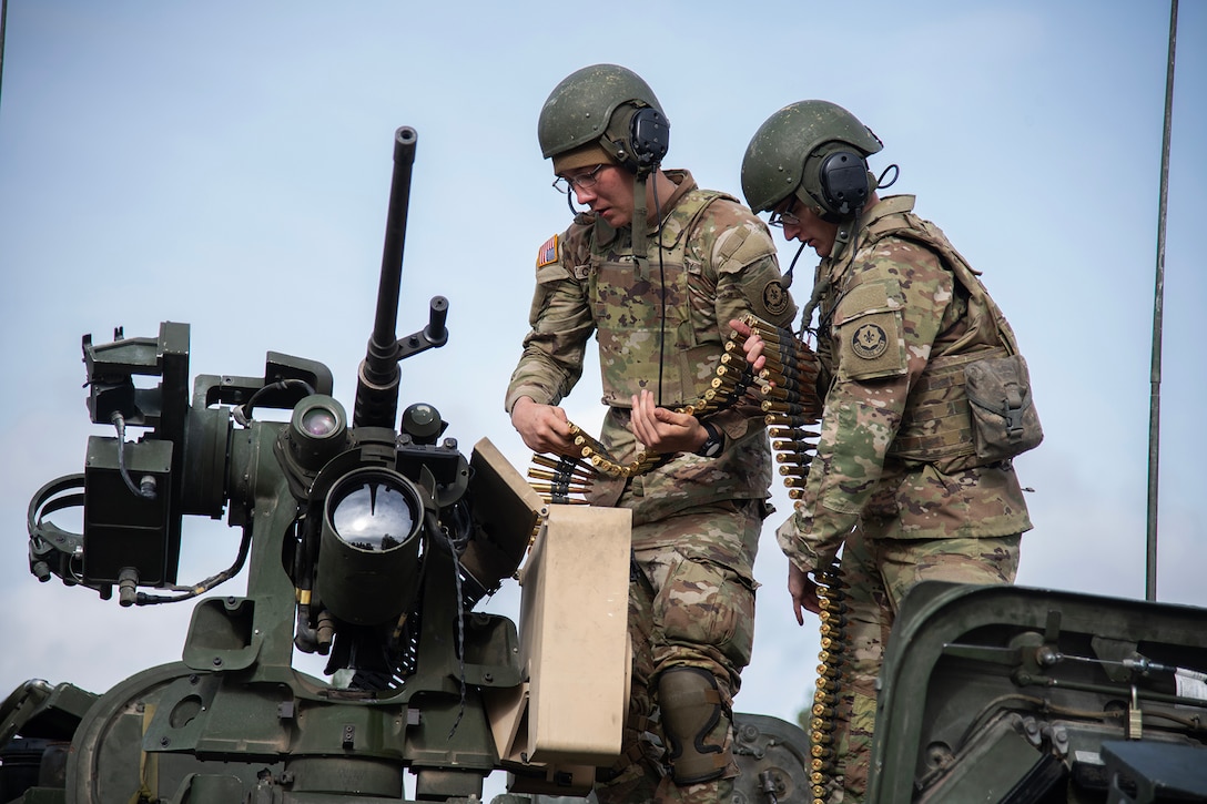 Two soldiers load ammunition into military machine gun.