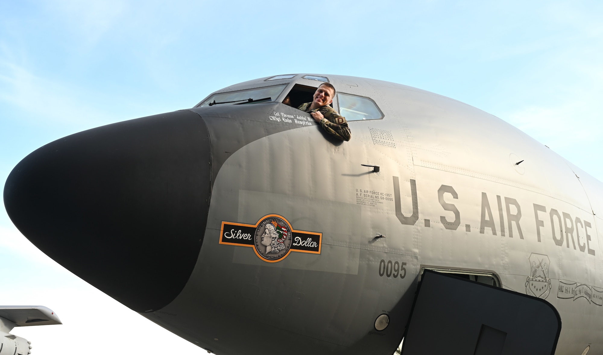U.S. Air Force Staff Sgt. Tyler Goldsborough, formerly 100th Aircraft Maintenance Squadron, now stationed at Tinker Air Force Base, Okla., sits in the pilot’s seat of a KC-135 Stratotanker after revealing the latest nose art in the 100th Air Refueling Wing’s heritage fleet of tankers during a dedication ceremony at Royal Air Force Mildenhall, England, Oct. 10, 2023. Goldsborough designed the updated nose art – the first to sport double-sided nose art, based on a Silver Dollar coin, and attended the ceremony to assist with the unveiling of his design. (U.S. Air Force photo by Karen Abeyasekere)