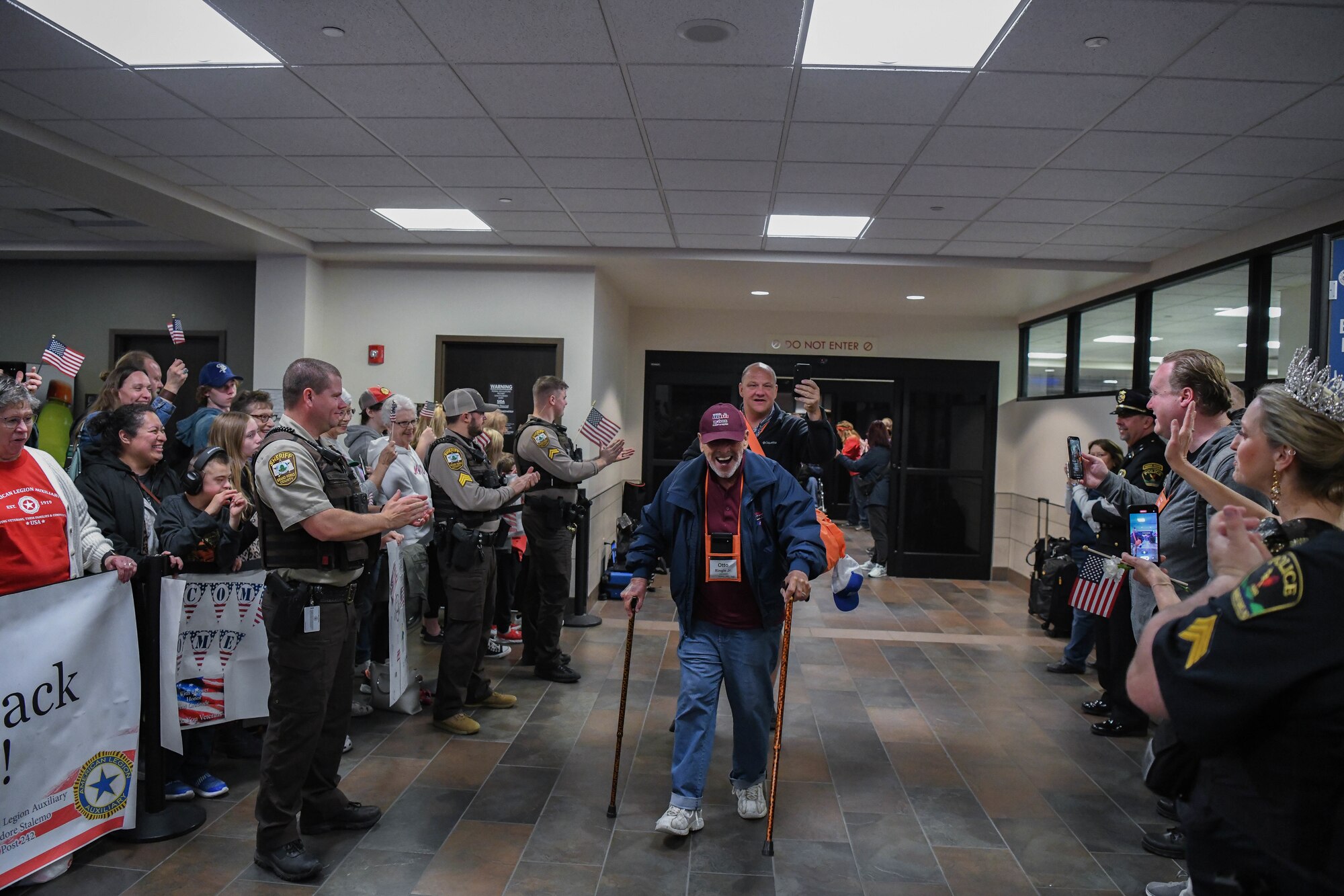 Veteran with two canes walks through a cheering crowd at an airport.