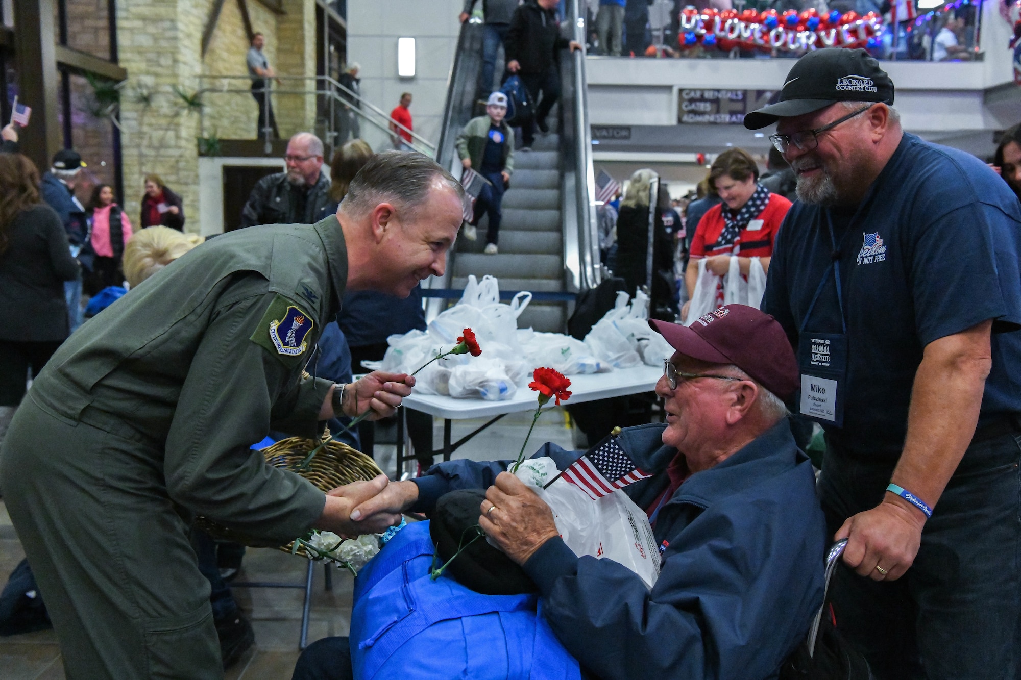 Military member in flight suit shakes hands with veteran in wheelchair.