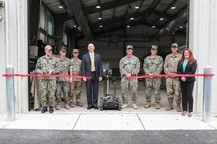 EOD T&T Program Board members along with NSWC IHD Technical Director Ashley Johnson (fourth from left), NSWC IHD Commanding Officer CAPT Steve Duba (fourth from right) and EOD Technology Center's Acting Department Head Denice Lee (far right) stand in front of the new Robot Building on NSWC IHD’s Stump Neck Annex as the ribbon is cut using a MTRS II robot.