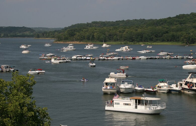Many boats sit on the water with trees in the background.