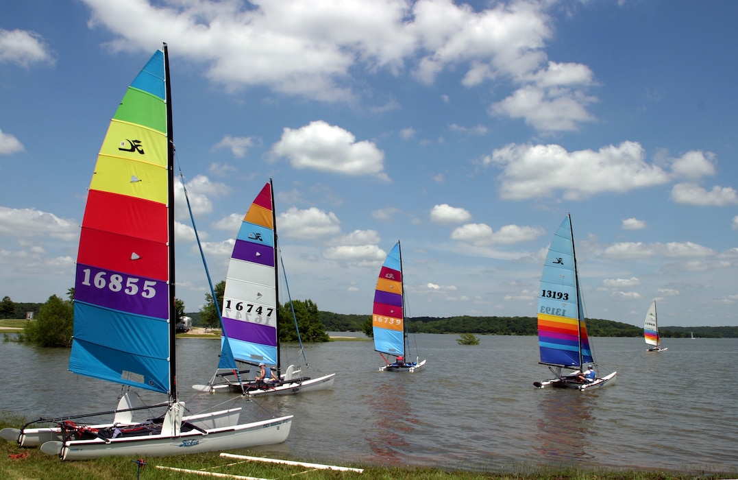 Several sailboats sit on the water with a cloudy sky in the background.