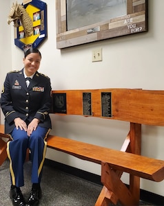 Woman in Army uniform poses on a bench