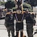 Two men in Army uniforms pose on either side of a horse mascot wearing Army shorts and suspenders