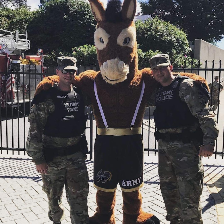 Two men in Army uniforms pose on either side of a horse mascot wearing Army shorts and suspenders
