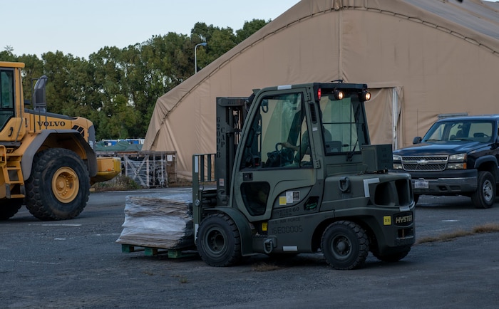 An Airman drives a forklift carrying supplemental structure defense equipment.