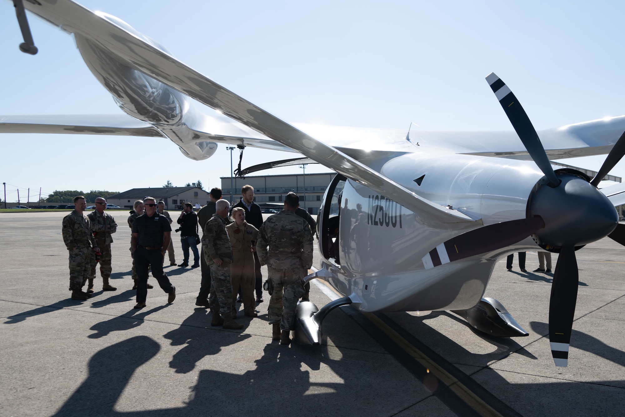 A group of people can be seen standing around an electric aircraft on a flight line.