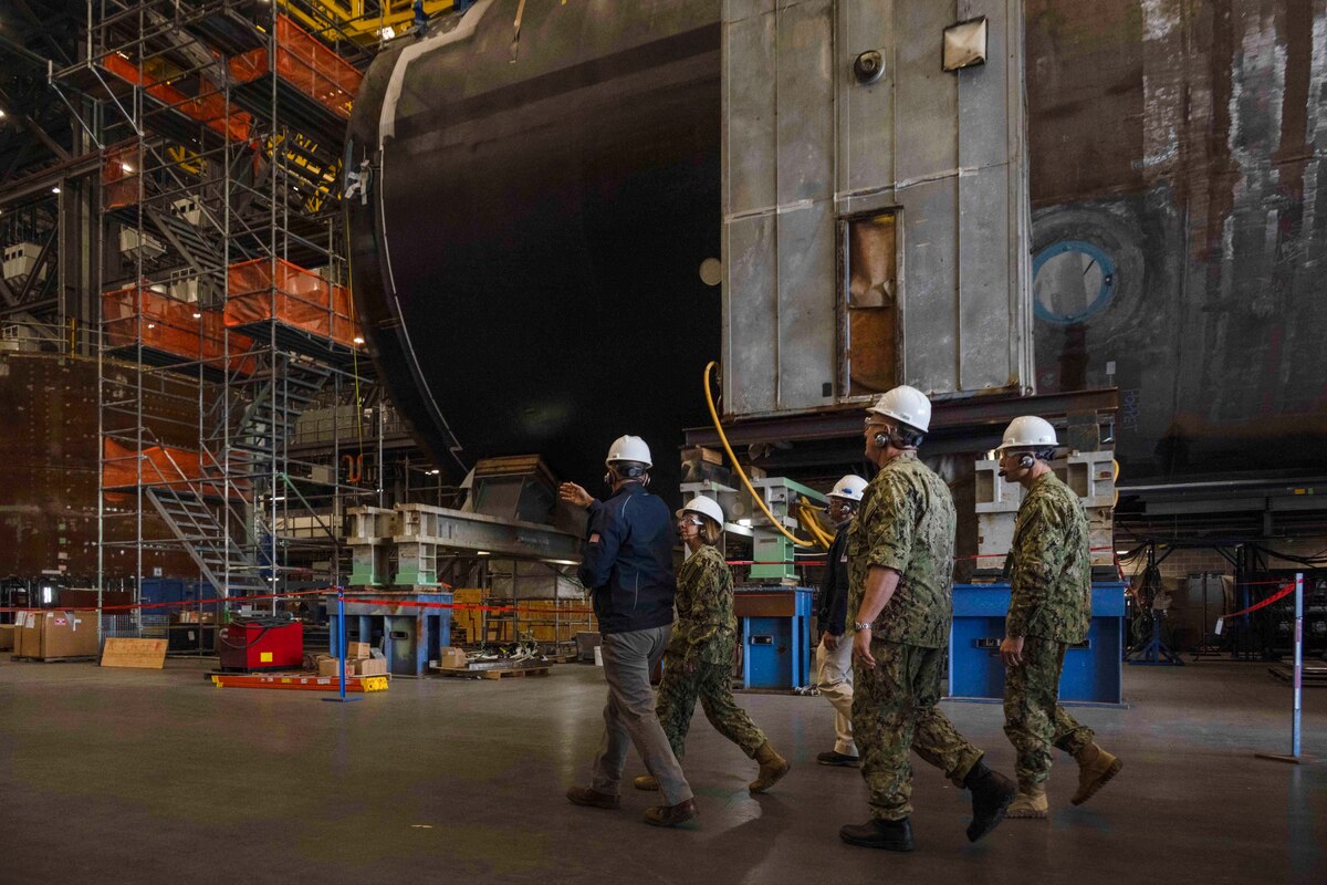 A group wearing hard hats walk in an industrial building.