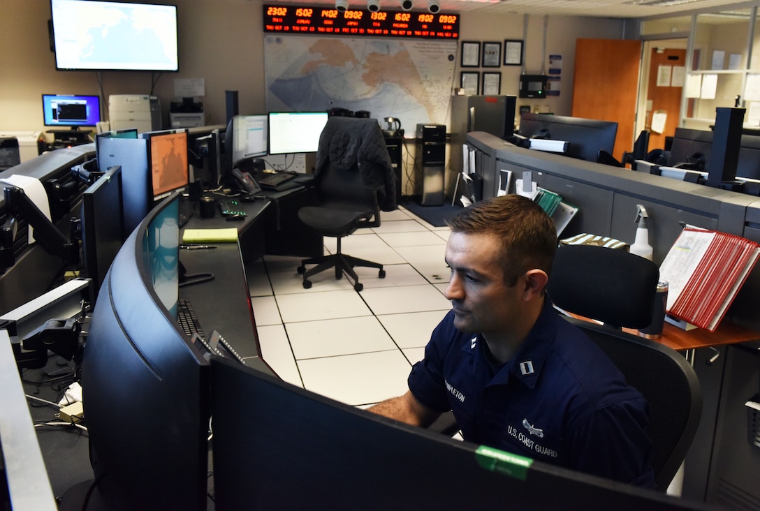 Two Seventeenth Coast guard District personnel talking in the command center in Juneau, Alaska, October 19, 2023. U.S. Coast Guard District Seventeen and the Tokyo Rescue Coordination Center conducted a joint planning exercise.