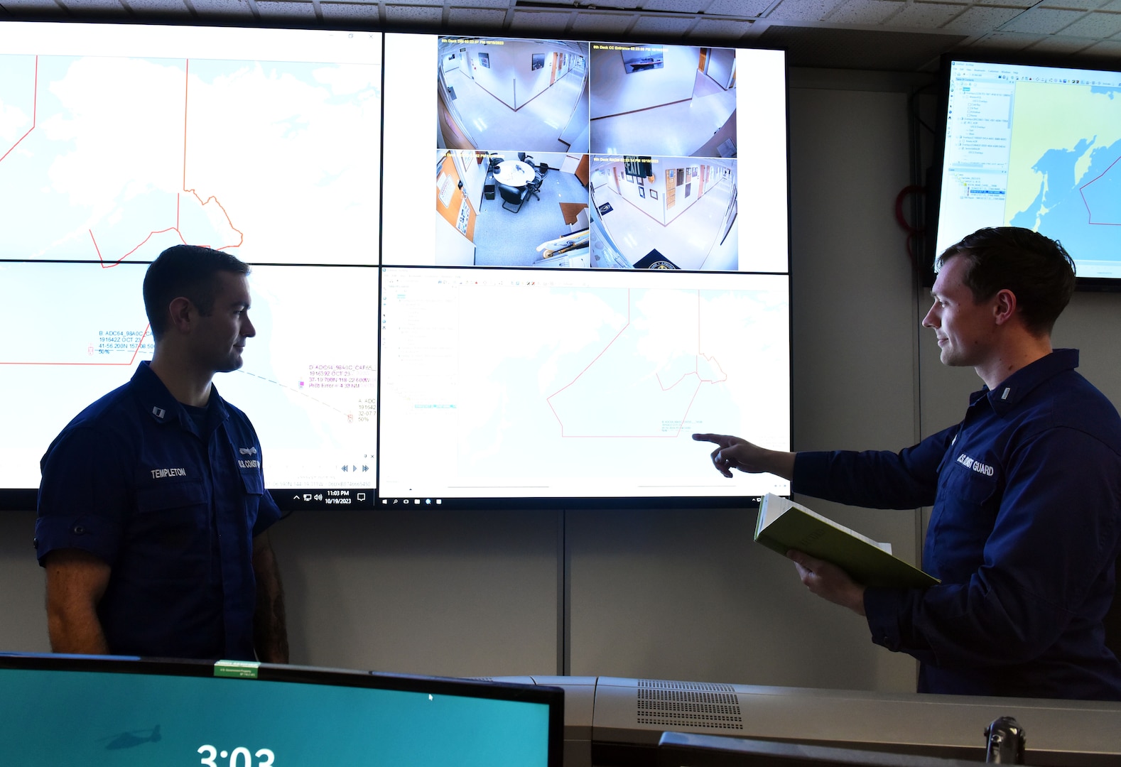 Two Seventeenth Coast guard District personnel talking in the command center in Juneau, Alaska, October 19, 2023. U.S. Coast Guard District Seventeen and the Tokyo Rescue Coordination Center conducted a joint planning exercise.