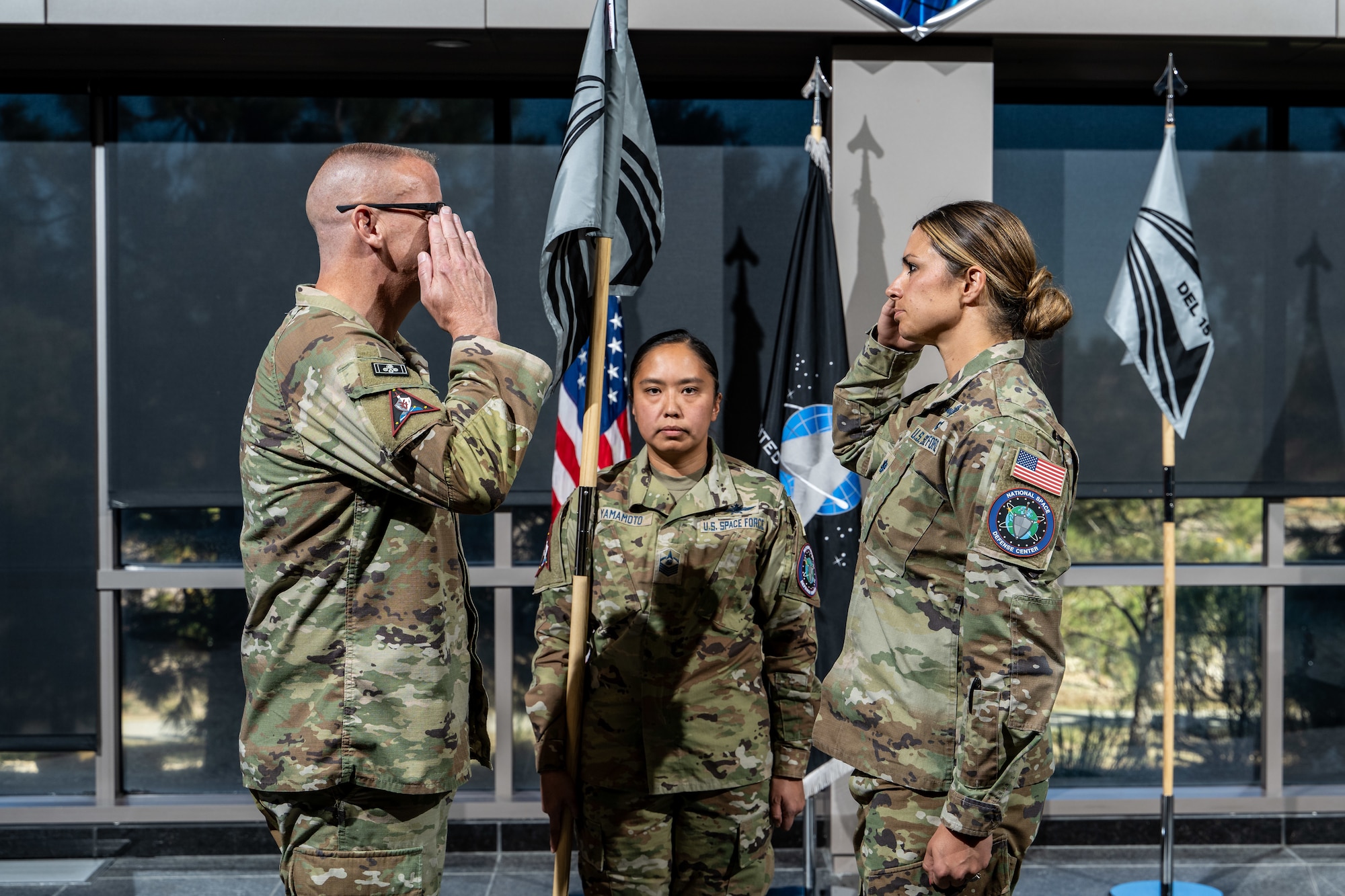 two military members salute eachother as one military member holds a guidon