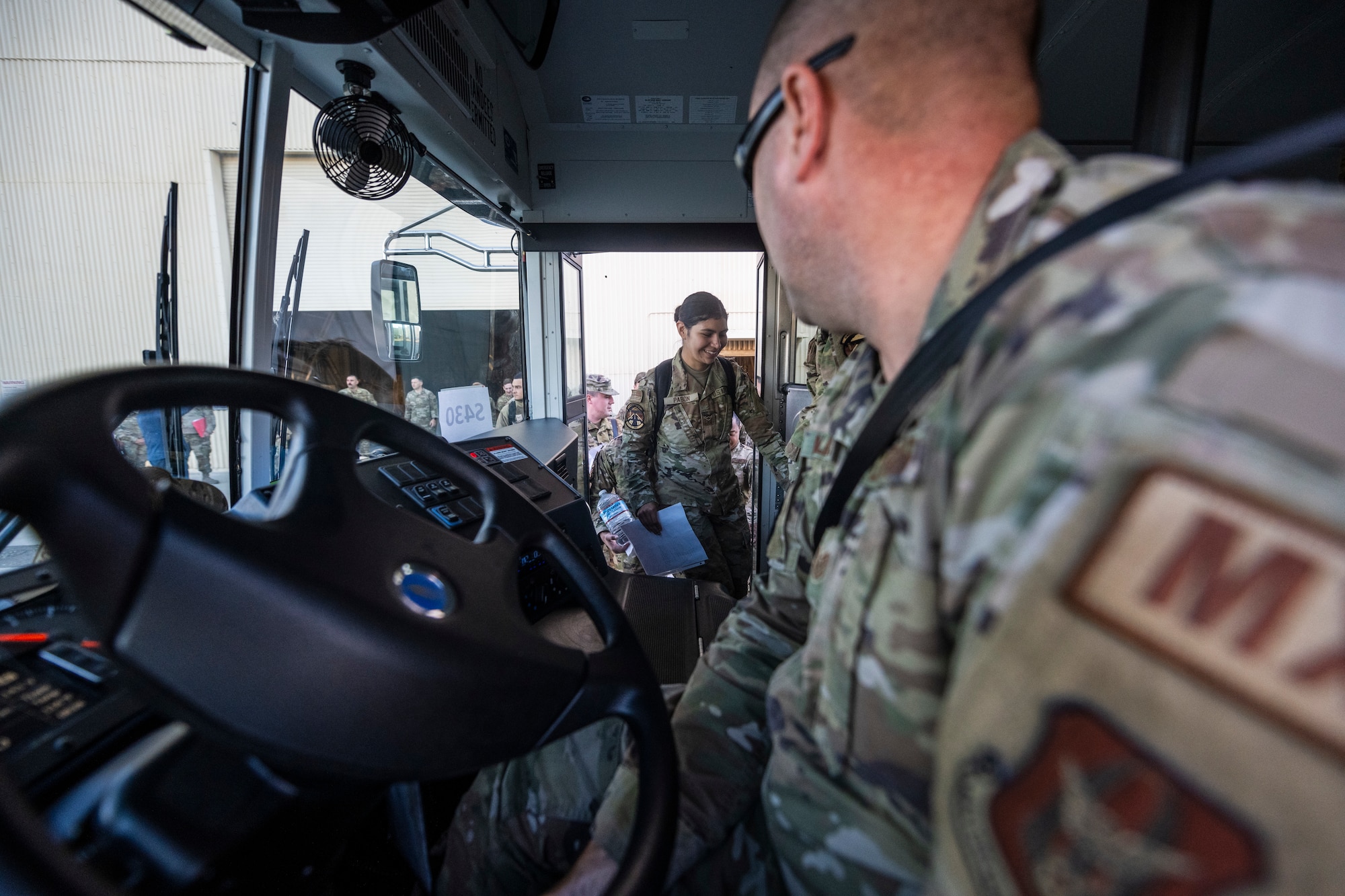 a man driving a parked bus looks at a woman walking onto the bus