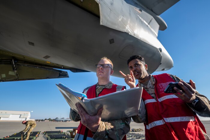 two men look at stuff under a large military aircraft
