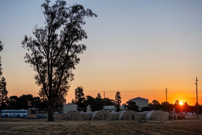 a wide image of a field that has a hospital made of tents and the sun is rising behind the horizon
