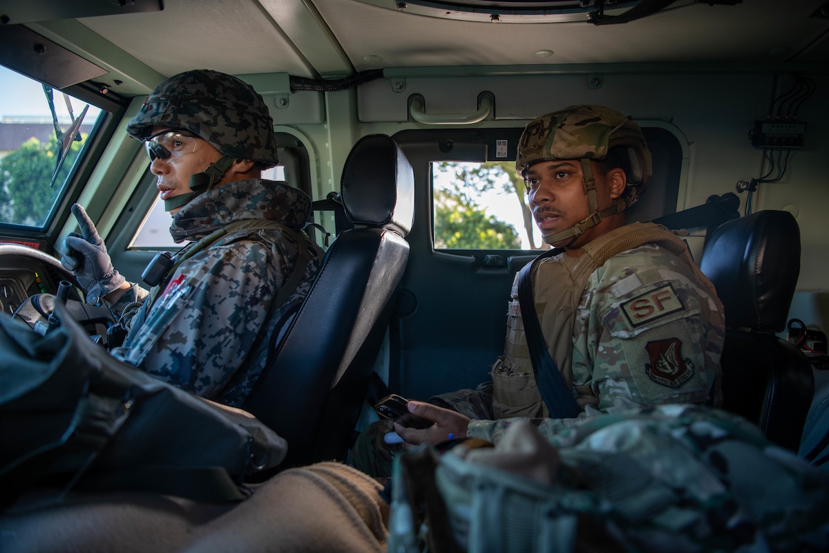 A Japan soldier and a U.S. Airman ride in a patrol vehicle.