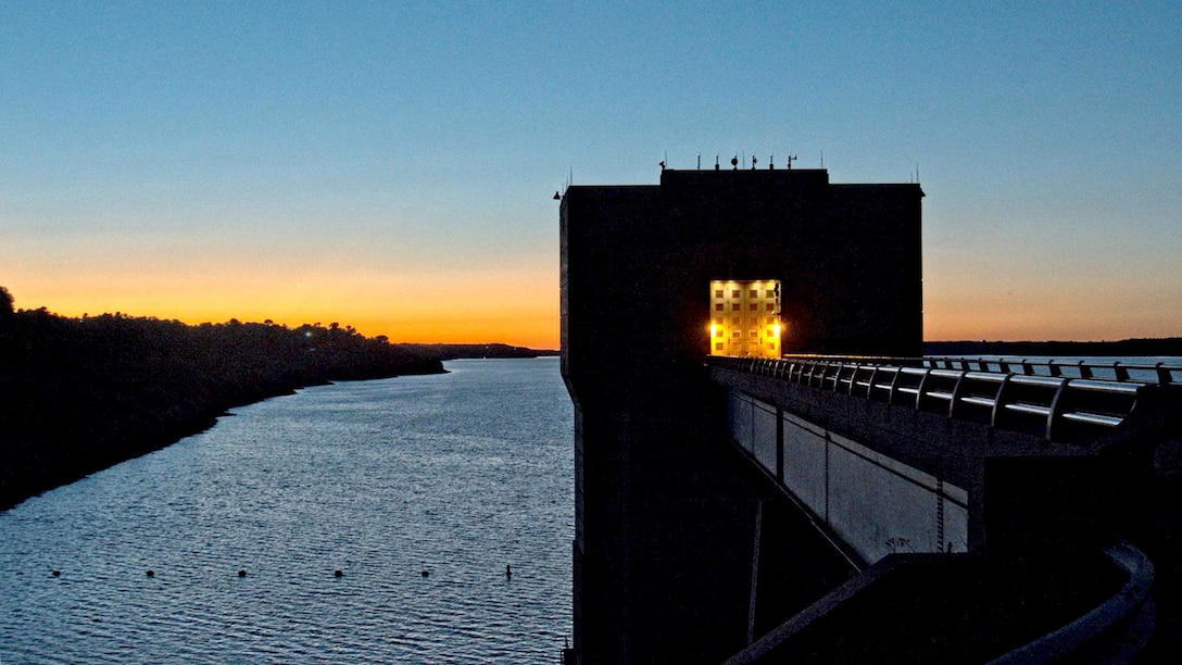 A yellow lit reservoir sits against an orange and blue sunset.