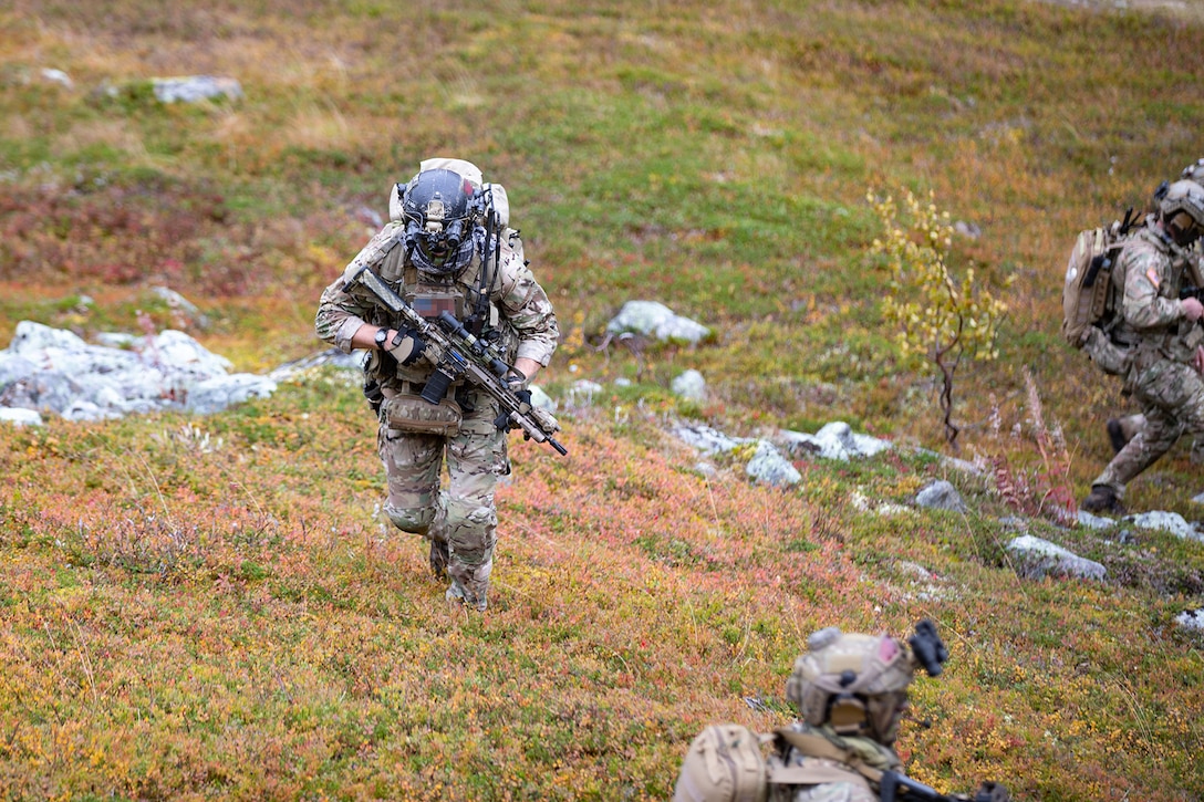 A solider carrying a weapon walks in a grassy area.