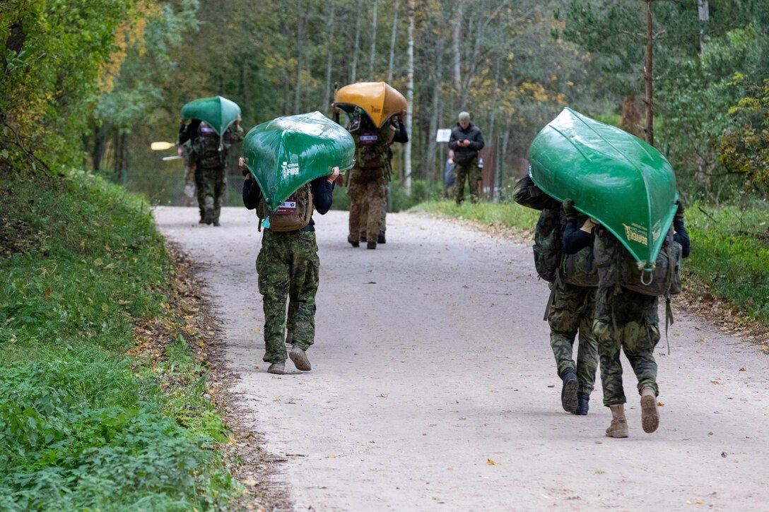 Soldiers carry canoes above their heads as they walk along a road.