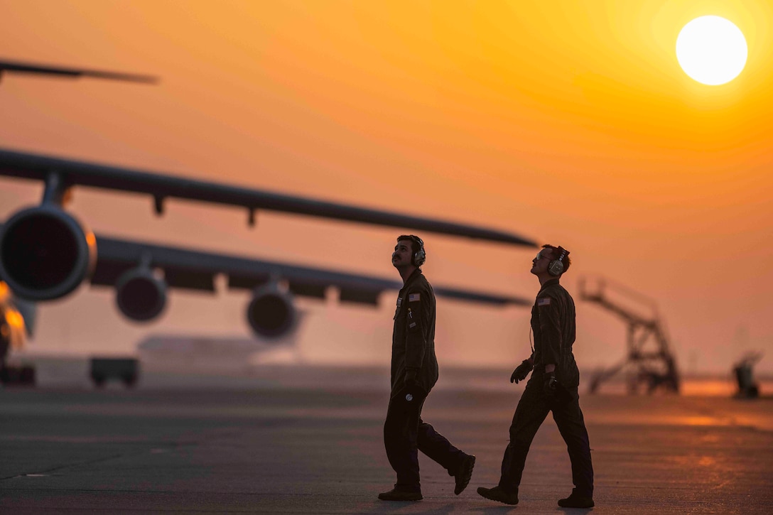 The sun shines on two airmen walking near parked aircraft.