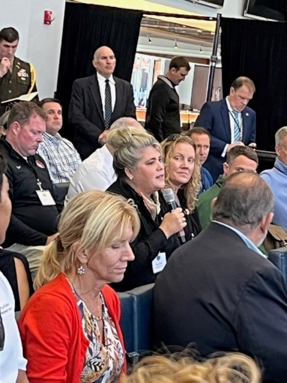 group of people sitting in rows of chairs with one woman holding a microphone.