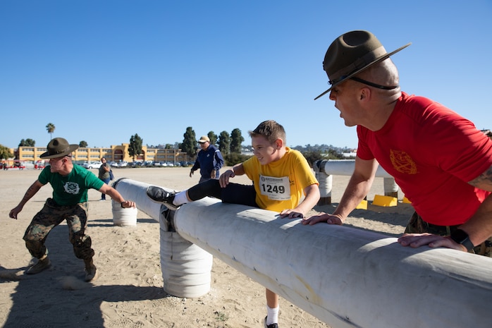 U.S. Marine Corps drill instructors with Recruit Training Regiment, motivate a participant of the Boot Camp Challenge as he navigates over an obstacle at Marine Corps Recruit Depot San Diego, Oct. 21, 2023. For the past 21 years the Boot Camp Challenge has offered a unique opportunity to the public to step into the shoes of a future Marine, guided by drill instructors to conquer a three-mile obstacle race and gain experience into what recruits go through during boot camp. (U.S. Marine Corps photo by Lance Cpl. Sarah Grawcock)