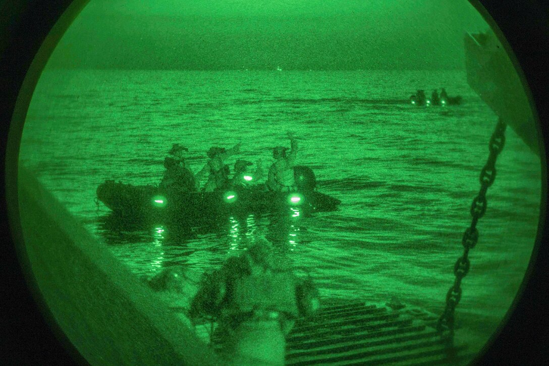 Marines ride in small rubber crafts as seen through a night vision lens.