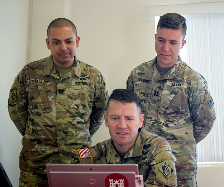Three uniformed Army officers gathered around a computer