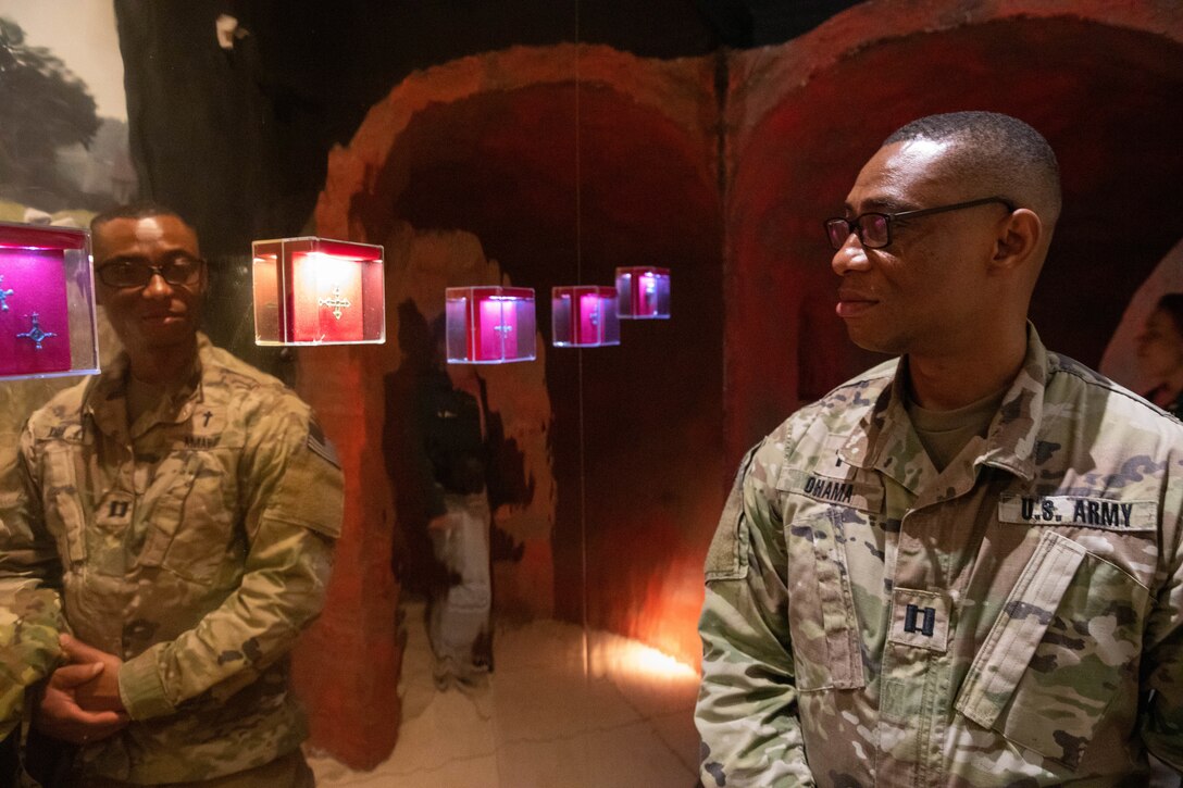 A soldier sees himself in a mirror as he walks through a dimly lit museum exhibit.