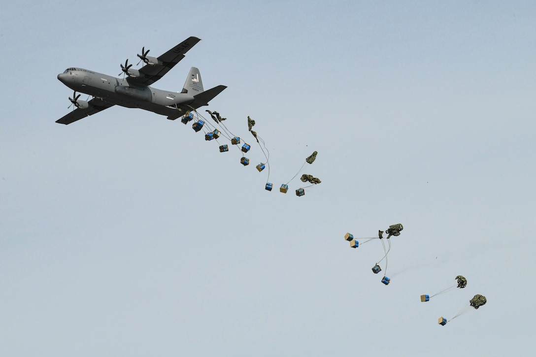 Containers attached to parachutes are dropped from a large aircraft.