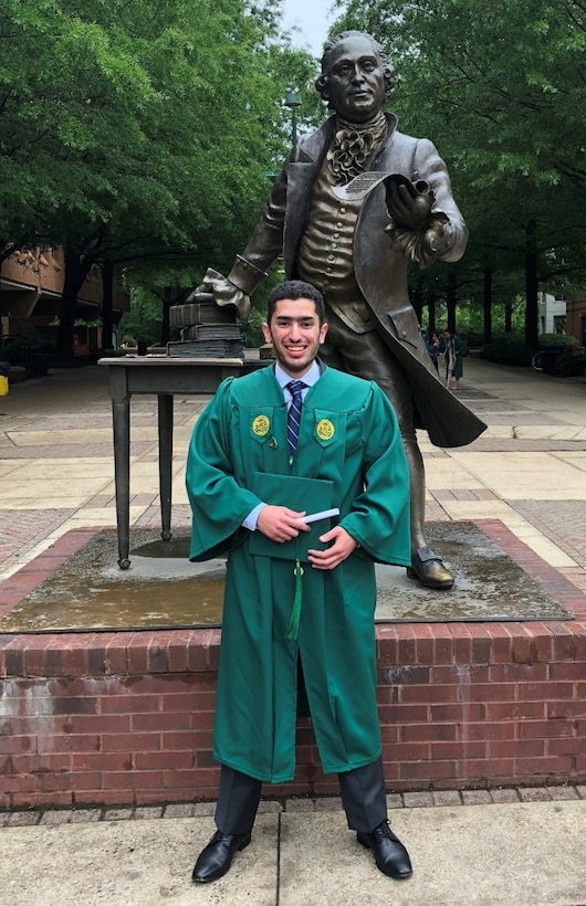 Omar Kaloub stands in front of a statue of George Mason wearing graduation attire.