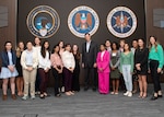 A group of men and women stand in front of the National Security Agency logo
