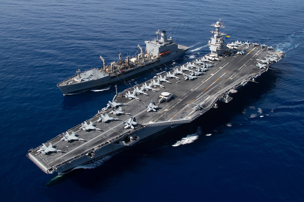 A military aircraft carrier is resupplied by military supply ship.