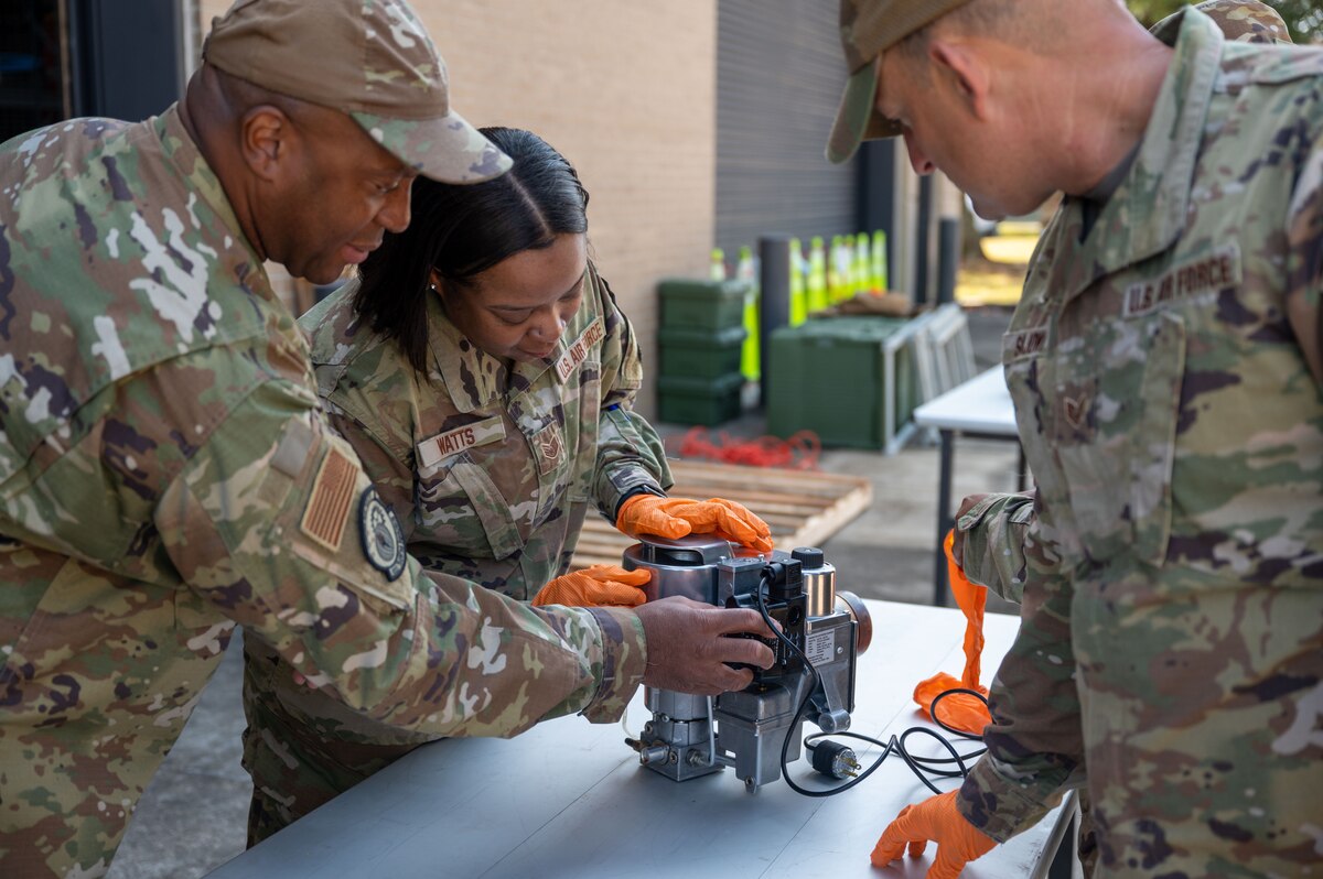Female Airman guided through the setup of a Babington burner by an instructor.