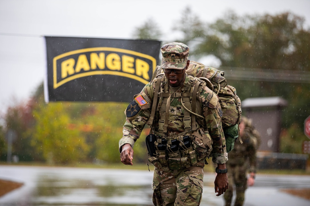 A uniformed soldier walks in the rain with a backpack. A banner behind the soldier reads, "Ranger."