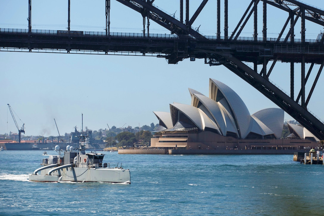 An unmanned surface vessel transits a body of water under a bridge with the Sydney Opera House to the right.