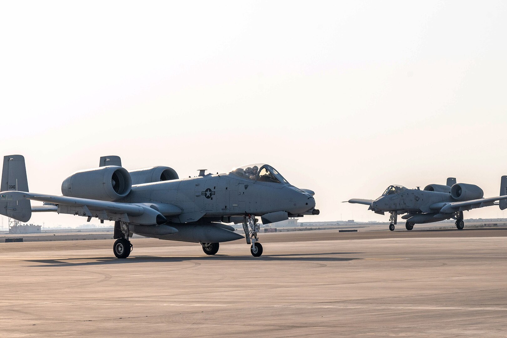 Two military aircraft sit are parked on a flightline.