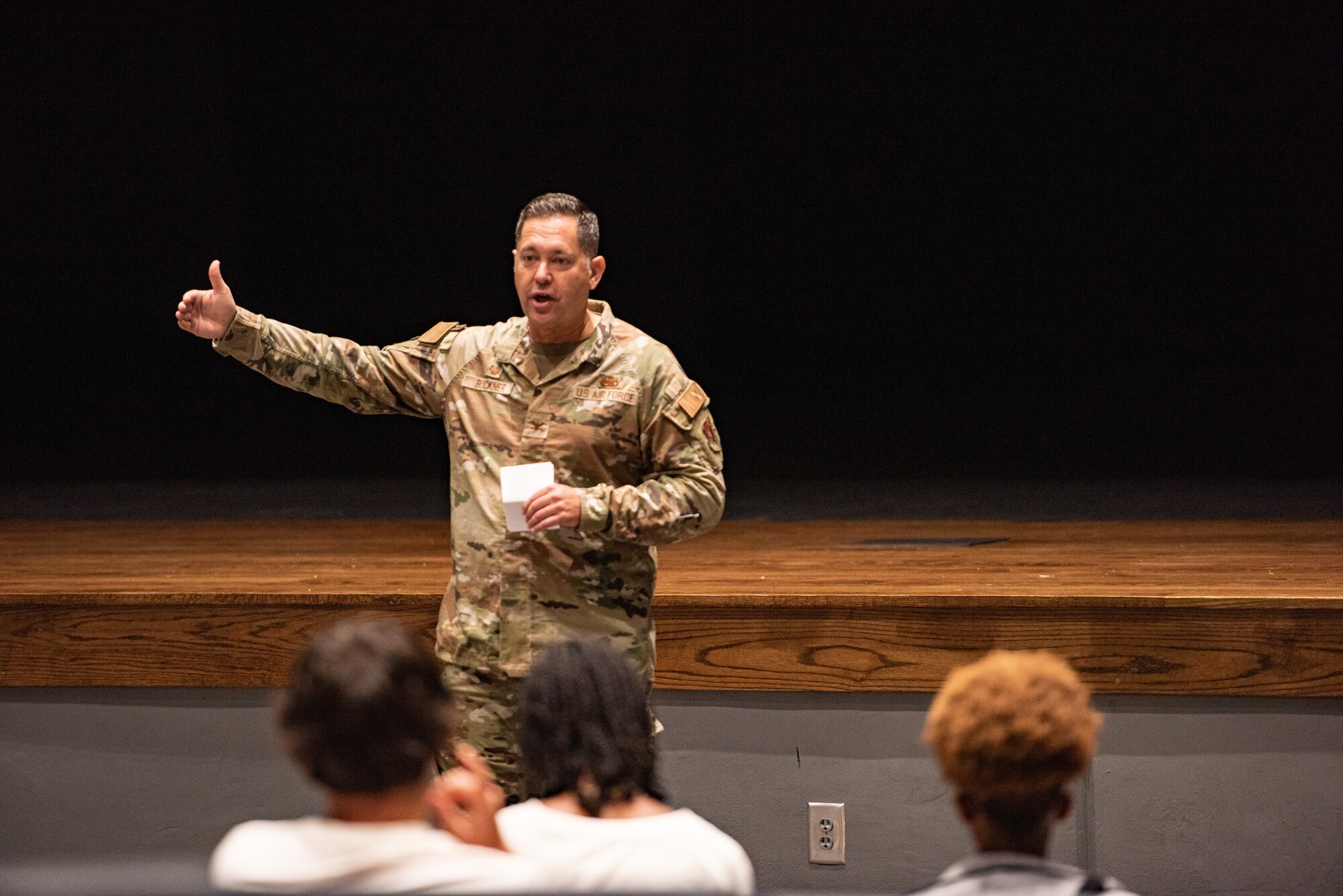 An Airmen stands in front of a crowd of student athletes in an auditorium