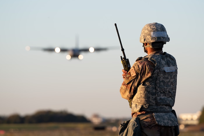 A man stands with a radio as a plane approaches for landing